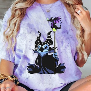 May include: Purple tie-dye t-shirt with a cartoon image of Stitch dressed as Maleficent from Disney's Sleeping Beauty. Stitch is holding a staff with a dragon on top.