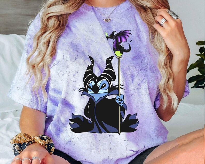 May include: Purple tie-dye t-shirt with a cartoon image of Stitch dressed as Maleficent from Disney's Sleeping Beauty. Stitch is holding a staff with a dragon on top.