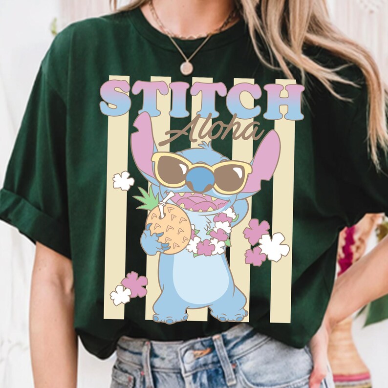 K&ouml;nnte beinhalten: Dunkelgr&uuml;nes T-Shirt mit einer Cartoon-Figur Stitch, die eine Sonnenbrille tr&auml;gt und eine Ananas h&auml;lt. Der Text "STITCH Aloha" wird &uuml;ber der Figur in einer bunten Schrift angezeigt, mit vertikalen Streifen im Hintergrund.