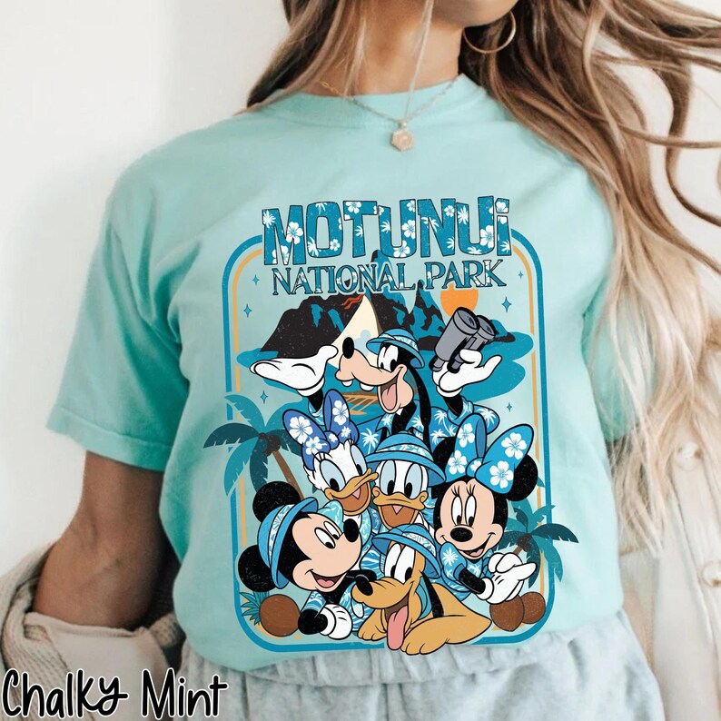 May include: A light blue t-shirt featuring a graphic of Disney characters, including Mickey, Minnie, Donald, Daisy, Goofy, and Pluto, with the text "Motunui National Park". The design includes palm trees and a mountain scene.
