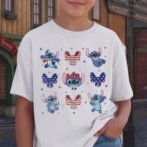 May include: White t-shirt with a repeating pattern of the character Stitch in various poses, alongside red, white, and blue bows and stars. The design has a patriotic theme, with Stitch wearing a cowboy hat and holding a sparkler.