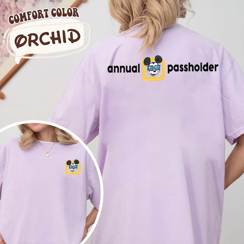 Puede incluir: Una camiseta de color lila claro con el texto "annual passholder" y un gr&aacute;fico de Mickey Mouse. La camiseta tambi&eacute;n tiene las palabras "Comfort Color" y "Orchid".
