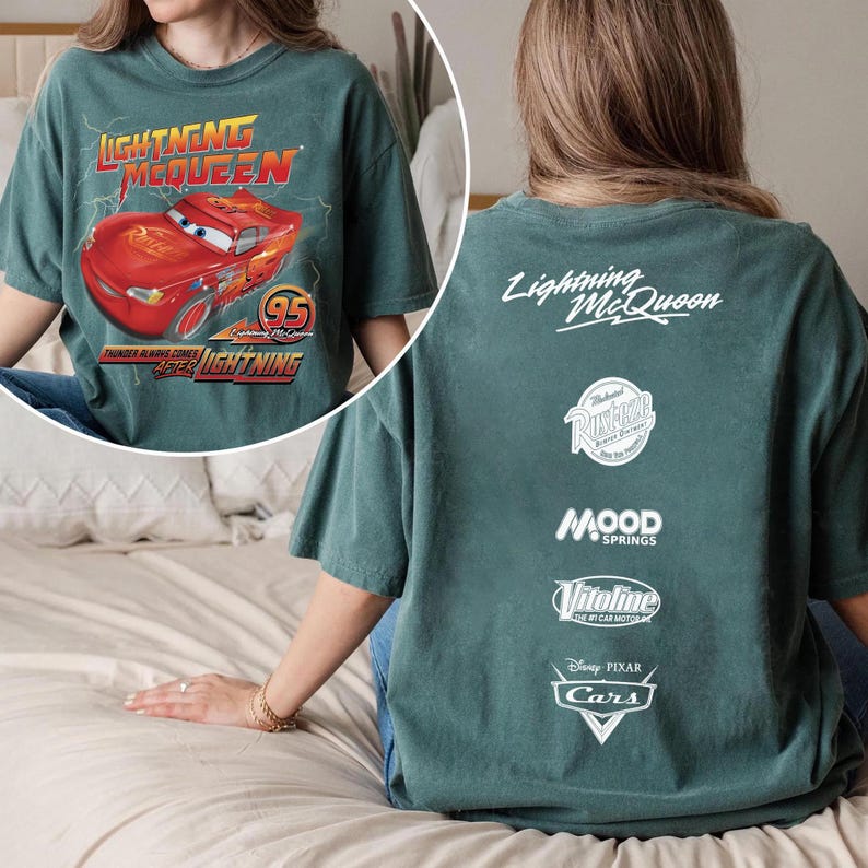 May include: Dark green t-shirt featuring Lightning McQueen from the Disney Pixar Cars movie. The front graphic shows the red race car with the text "Lightning McQueen" and "95". The back of the shirt has the text "Lightning McQueen" and various logos.