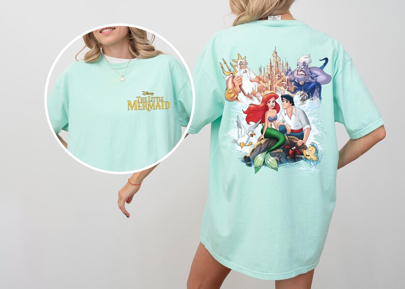 May include: A light blue t-shirt with a graphic print of characters from the Disney movie The Little Mermaid. The text "The Little Mermaid" is printed in gold on the front of the shirt.