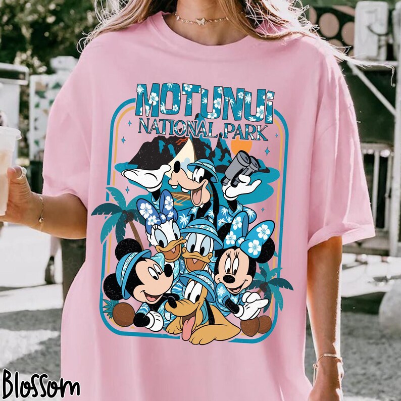 May include: Pink t-shirt featuring a graphic of Disney characters, including Mickey, Minnie, Donald, Daisy, Goofy, and Pluto, with the text "Motunui National Park." The design is framed with a blue border and palm trees.