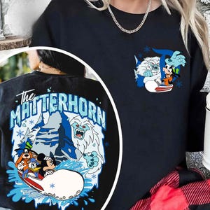 May include: Black sweatshirt featuring a colorful graphic of cartoon characters on a watercraft, with the text "The Matterhorn" on the back. The front has a smaller graphic of the same characters. The design includes blue, white, and orange accents.