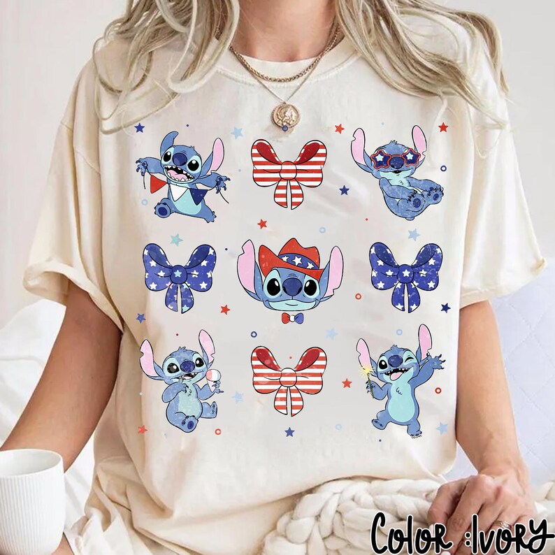 May include: Ivory-coloured t-shirt with a repeating pattern of the character Stitch in various poses, alongside red, white, and blue bow ties and stars. The shirt has a relaxed fit and short sleeves. The text "Color Ivory" is at the bottom.