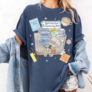 Puede incluir: Camiseta azul marino con un dise&ntilde;o de dibujos animados para el D&iacute;a de los Profesionales Administrativos 2026. El dise&ntilde;o incluye un conejo, papeleo, una taza de caf&eacute; y las palabras "Assistant Mayor".