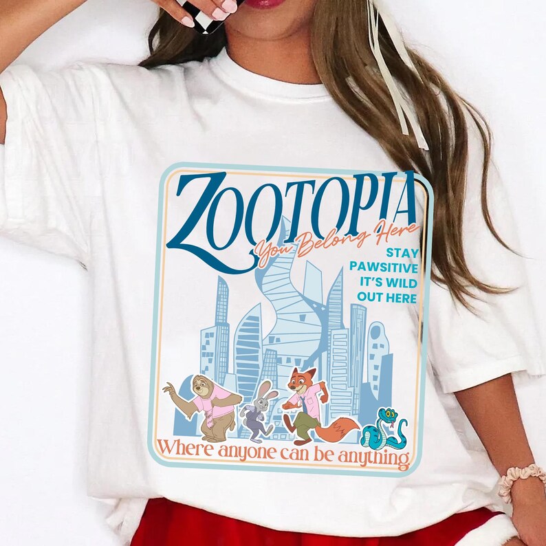 Puede incluir: Camiseta blanca con un dise&ntilde;o gr&aacute;fico de la pel&iacute;cula Zootopia. El dise&ntilde;o incluye el t&iacute;tulo "Zootopia", personajes de dibujos animados y la frase "Where anyone can be anything". La camiseta tiene cuello redondo y mangas cortas.