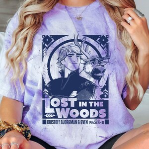 Puede incluir: Camiseta morada te&ntilde;ida con un dise&ntilde;o de la pel&iacute;cula Frozen II de Disney. El dise&ntilde;o incluye el texto "LOST IN THE WOODS" e im&aacute;genes de Kristoff Bjorgman y Sven. La camiseta tiene cuello redondo y mangas cortas.