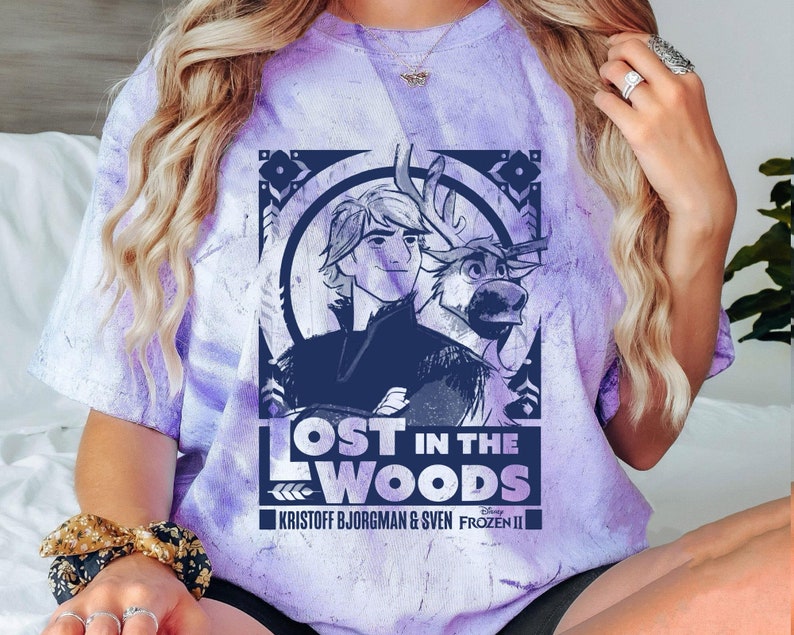 Puede incluir: Camiseta morada te&ntilde;ida con un dise&ntilde;o de la pel&iacute;cula Frozen II de Disney. El dise&ntilde;o incluye el texto "LOST IN THE WOODS" e im&aacute;genes de Kristoff Bjorgman y Sven. La camiseta tiene cuello redondo y mangas cortas.