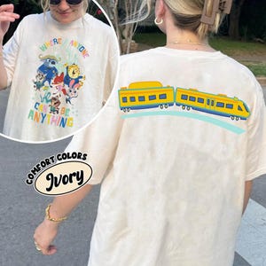 Pu&ograve; includere: T-shirt Comfort Colors color avorio con una grafica colorata sul davanti con personaggi dei cartoni animati e la scritta "WHERE ANYONE CAN BE ANYTHING". Il retro della maglietta presenta un disegno di un treno giallo e blu.