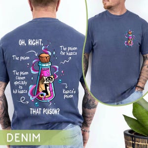 May include: A denim blue t-shirt with a cartoon image of a potion bottle and text that reads "OH, RIGHT. The poison. The poison chosen specially to kill kuzco. THAT POISON?" and "The poison for kuzco" and "Kuzco's poison".