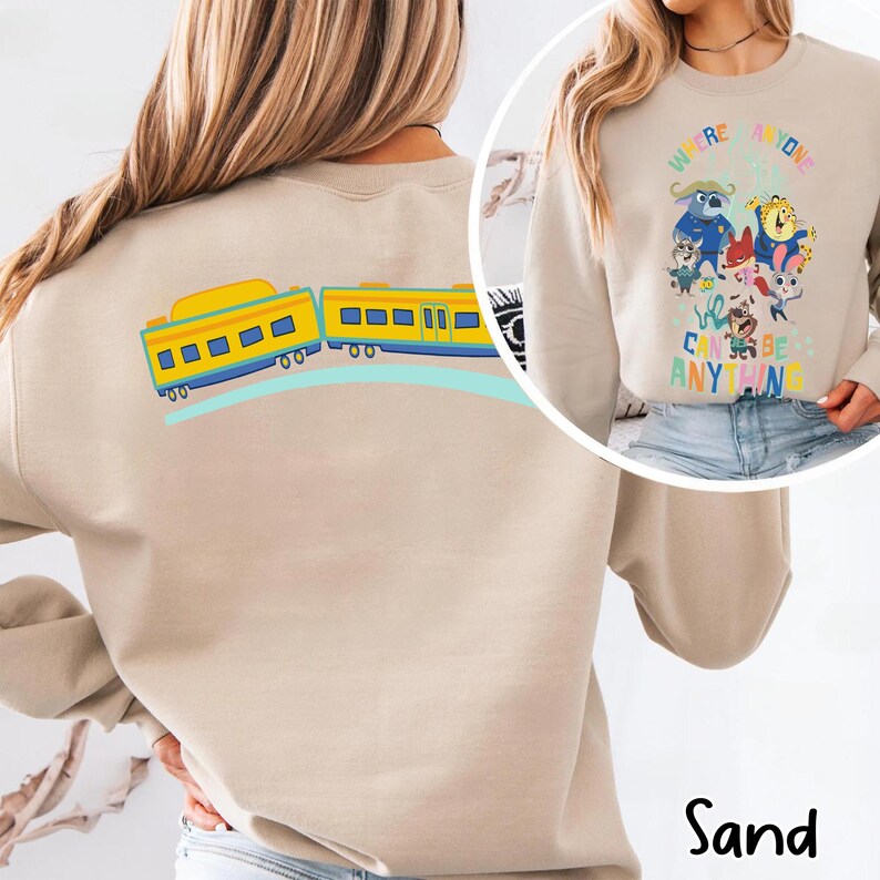 Pu&ograve; includere: Felpa color sabbia con una grafica colorata di un treno sul retro e un design di personaggi dei cartoni animati sul davanti. Il design frontale include il testo "We're Anyone, We Can Be Anything."