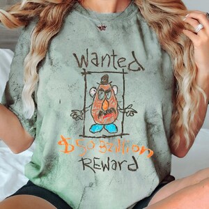 K&ouml;nnte beinhalten: Gr&uuml;nfarbenes T-Shirt mit Batik-Muster und einer Comic-Zeichnung von Mr. Potato Head mit dem Text "Wanted 50 Milliarden Dollar Belohnung".