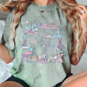 May include: Green tie-dye t-shirt with a colourful graphic of Disney World landmarks and the words "Disney World". The design includes various attractions in pastel colours.