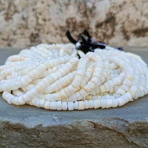 May include: A close-up of a pile of white shell beads. The beads are square shaped and have a smooth, polished finish.