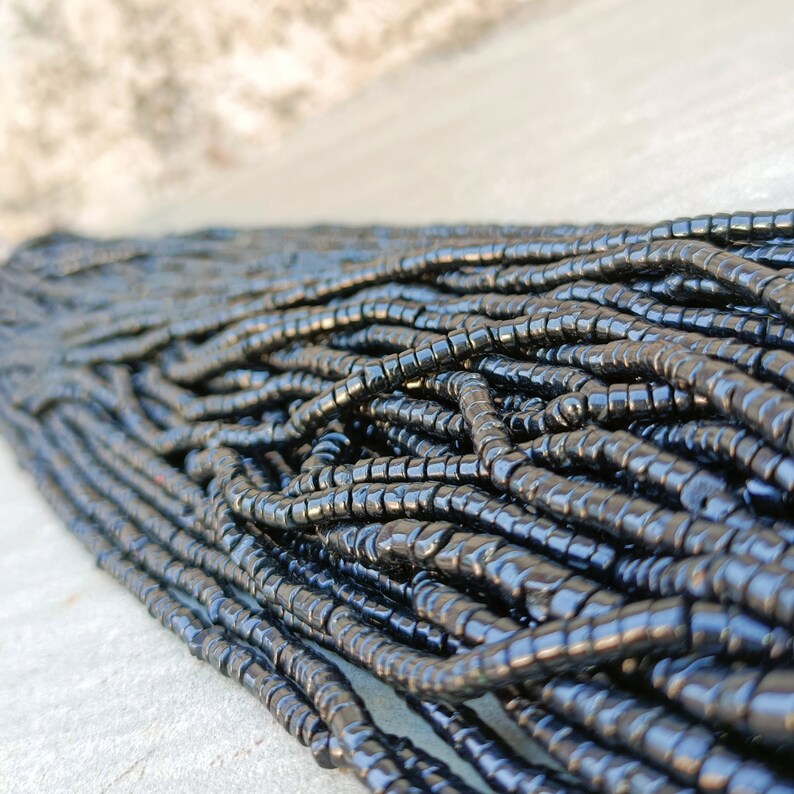 K&ouml;nnte beinhalten: Nahaufnahme einer gro&szlig;en Menge schwarzer Glasperlen. Die Perlen sind klein und zylindrisch und liegen lose in einem Haufen.