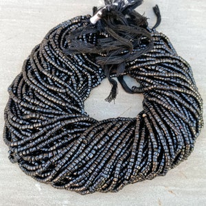 K&ouml;nnte beinhalten: Eine gro&szlig;e Schnur schwarzer Perlen, wahrscheinlich aus Onyx oder Obsidian, ist zu einem Kreis gewickelt. Die Perlen sind klein und gleichm&auml;&szlig;ig gro&szlig;, was der Schnur ein glattes und poliertes Aussehen verleiht.