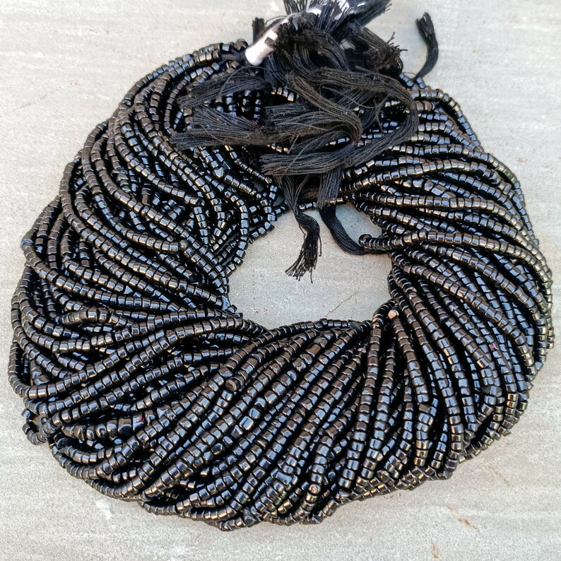 K&ouml;nnte beinhalten: Eine gro&szlig;e Schnur schwarzer Perlen, wahrscheinlich aus Onyx oder Obsidian, ist zu einem Kreis gewickelt. Die Perlen sind klein und gleichm&auml;&szlig;ig gro&szlig;, was der Schnur ein glattes und poliertes Aussehen verleiht.