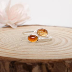 May include: A silver ring with two oval-shaped amber gemstones. The ring is designed to wrap around the finger.