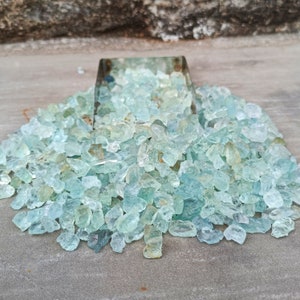 Puede incluir: Un mont&oacute;n grande de piedras preciosas de aguamarina azul claro, algunas de las cuales est&aacute;n en un peque&ntilde;o contenedor de metal.