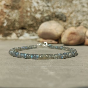 Puede incluir: Un brazalete de plata con una fila de cuentas de labradorita azul grisáceo iridiscente.