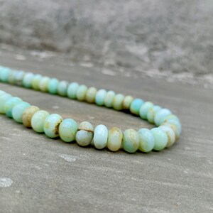 May include: A strand of light blue and tan gemstone beads. The beads are oval-shaped and vary in size, creating a textured appearance. The beads are strung together, forming a necklace or bracelet.
