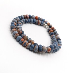 K&ouml;nnte beinhalten: Eine Kette aus blauen und orangefarbenen Edelsteinperlen mit einem silbernen Verschluss.