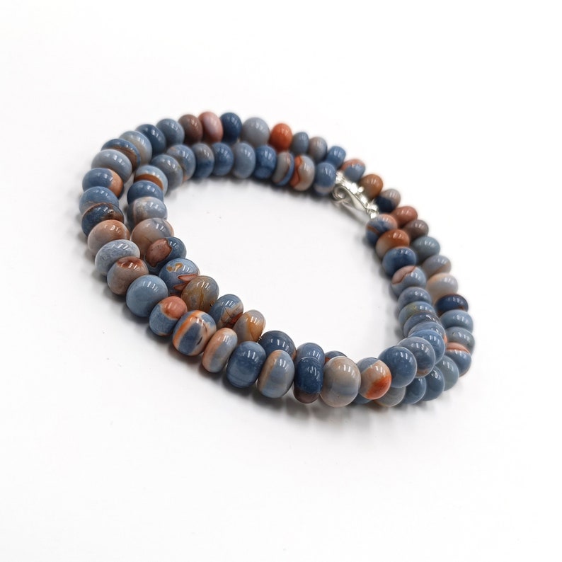 K&ouml;nnte beinhalten: Eine Kette aus blauen und orangefarbenen Edelsteinperlen mit einem silbernen Verschluss.