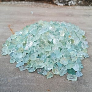 Puede incluir: Un mont&oacute;n de piedras preciosas de aguamarina azul claro, tambi&eacute;n conocidas como cristales de aguamarina, sobre una superficie gris. Los cristales son de varios tama&ntilde;os y formas.