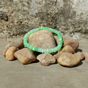 May include: A green gemstone bracelet made of round beads. The bracelet is resting on a pile of small, smooth rocks.