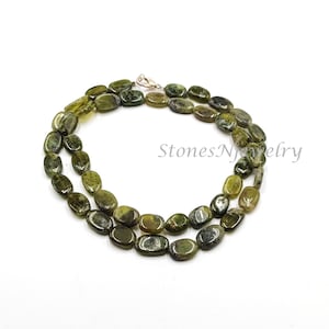 以下が含まれることがあります： オリーブグリーンの楕円形ビーズのネックレス。ビーズは研磨仕上げで、シルバーの留め金で繋がれています。「StonesNjewelry」の文字が画像に表示されています。