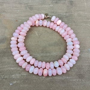 May include: A pink opal bead necklace with a silver clasp. The beads are oval shaped and have a slight iridescent sheen.