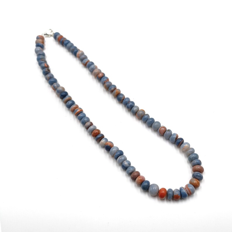 K&ouml;nnte beinhalten: Eine Halskette aus blauen, braunen und orangefarbenen Perlen mit Mustern. Die Halskette ist aus Naturstein und hat einen silbernen Verschluss.