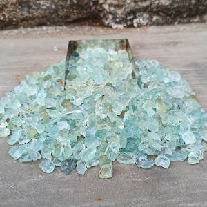 Puede incluir: Un mont&oacute;n grande de piedras preciosas de aguamarina azul claro, algunas de las cuales est&aacute;n en un peque&ntilde;o contenedor de metal.