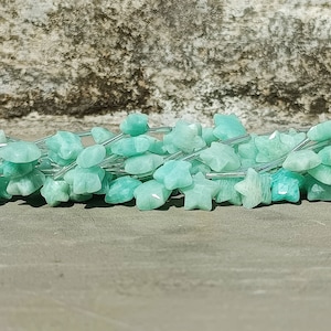 May include: A pile of light green star-shaped gemstone beads. The beads are strung on silver wire.