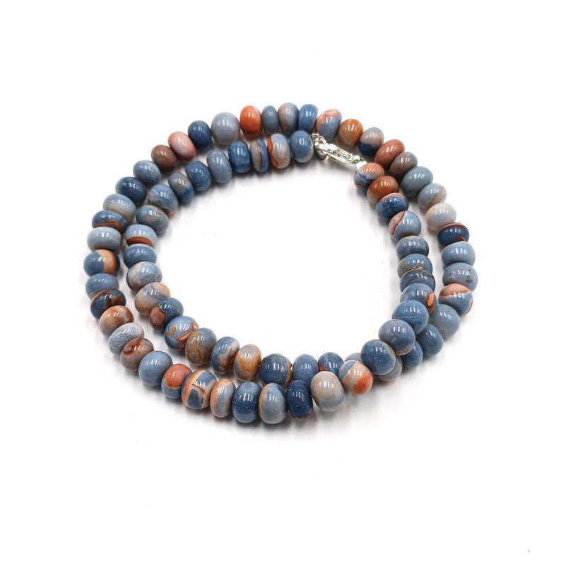 K&ouml;nnte beinhalten: Eine Kette aus blauen und orangefarbenen Edelsteinperlen mit einem silbernen Verschluss. Die Perlen sind rund und haben ein marmoriertes Muster.