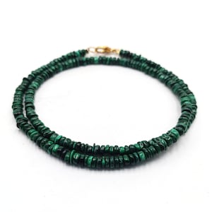 May include: A double strand necklace made of green malachite beads. The beads are small and round, and the necklace is simple and elegant.