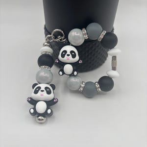 May include: A panda-themed keychain and bracelet set. The keychain features a panda charm and a beaded strand with black, white, and gray beads. The bracelet has similar beads with rhinestone accents. The panda charms are black and white.