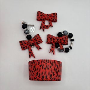 Könnte beinhalten: Eine Sammlung von Halloween-Accessoires, darunter rote Stoffschleifen mit schwarzen Schädel- und Spinnenmustern sowie Armbänder mit schwarzen und silbernen Perlen. Ein roter Behälter mit einem schwarzen Halloween-Muster ist ebenfalls vorhanden.