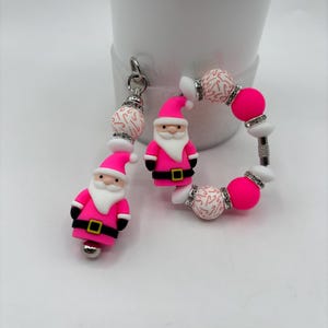 以下が含まれることがあります： ピンクと白のクリスマスをテーマにしたジュエリーセット。ブレスレットとチャームが含まれています。ブレスレットにはピンクのビーズ、キャンディケーンのデザインの白いビーズ、サンタクロースのチャームがあります。チャームはサンタクロースのデザインです。お祝いにぴったりのカラフルなセットです。