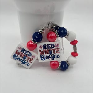 May include: A patriotic bracelet with red, white, and blue beads. The bracelet features square charms with the text "Red White Boujee" in red, white, and blue. The beads are a mix of solid colors and star-patterned blue beads.