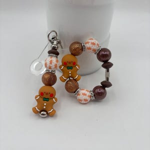 May include: A gingerbread man keychain and bracelet set. The keychain features a gingerbread man charm and decorative beads in brown, white, and gold. The bracelet has similar beads and a gingerbread man charm. The set is festive and colorful.