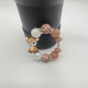May include: A brown and white patterned beaded bracelet with a small deer charm and silver beads.