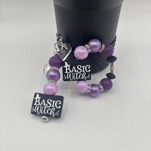 Può includere: Un set di braccialetto e portachiavi con la scritta "Basic Witch". Il braccialetto e il portachiavi presentano perline viola e rosa chiaro con dettagli argentati. Il portachiavi ha un ciondolo a forma di cuore.
