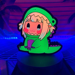 May include: A neon green cartoon character in a dinosaur costume with a black outline. The character has blonde hair, pink cheeks, and a small mouth. The background is a neon blue and purple landscape.