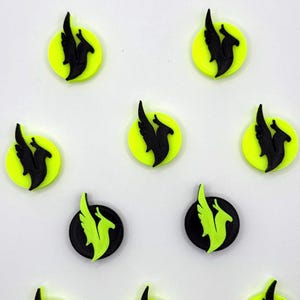 Può includere: Una collezione di piccoli abbellimenti circolari. Ognuno ha una silhouette nera di una creatura alata su uno sfondo giallo neon o nero. Il design è ripetuto nell'immagine, creando un motivo.