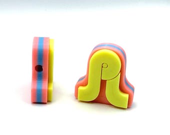 Puede incluir: Dos pequeños componentes de plástico multicolor con un diseño en capas de color rosa coral, azul claro y amarillo brillante. Una pieza está en posición vertical, mientras que la otra está de lado, revelando un pequeño orificio circular.