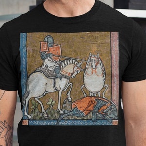 Pode incluir: Uma camiseta preta com uma ilustração medieval de um cavaleiro a cavalo matando um dragão. A ilustração é em um estilo colorido e estilizado.